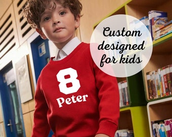 May include: A red sweatshirt with a white number 8 and the name Peter printed on the front. The sweatshirt is worn by a young boy with curly brown hair. The text "Custom designed for kids" is superimposed on the image.