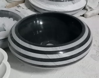 May include: A black and white striped round ceramic sink. The sink is made of a smooth, polished material and has a wide, shallow bowl.
