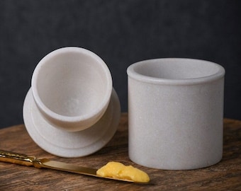 May include: A white marble butter dish with a lid and a small knife with a pat of butter on it.