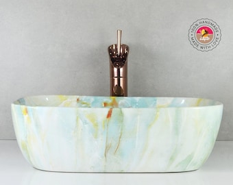 May include: A white ceramic bathroom sink with a light blue and yellow marbled design. The sink is oval shaped and has a single faucet.