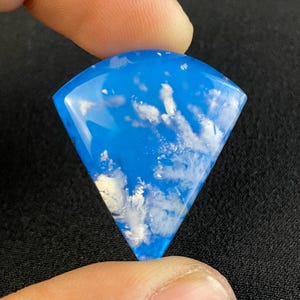 May include: A blue and white agate cabochon with a fan shape. The agate has a cloudy blue colour with white dendritic inclusions.