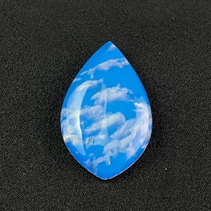 May include: A teardrop-shaped cabochon with a blue and white agate pattern. The stone has a cloudy, sky-like appearance.