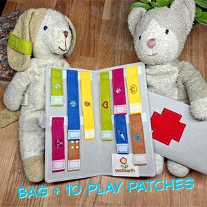 Puede incluir: Un juego de juguetes de peluche para perros y gatos con un libro de fieltro gris con parches de fieltro de colores con diseños bordados. El libro tiene el texto "BAG + 10 PLAY PATCHES" y está junto a una bolsa de fieltro gris con una cruz roja.