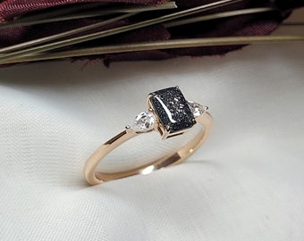May include: A gold ring with a black rectangular center stone and two smaller pear-shaped stones on either side.