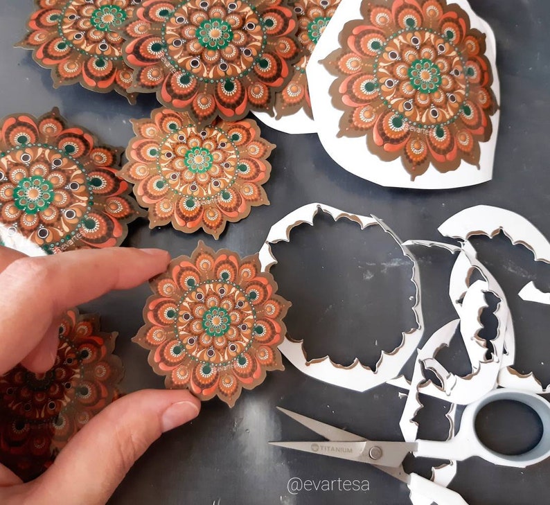 K&ouml;nnte beinhalten: Ein Satz von f&uuml;nf runden Mandala-Aufklebern mit filigranen Designs in Braun-, Orange- und Gr&uuml;nt&ouml;nen. Die Aufkleber befinden sich auf wei&szlig;em Untergrund und wurden mit einem Bastelmesser ausgeschnitten.