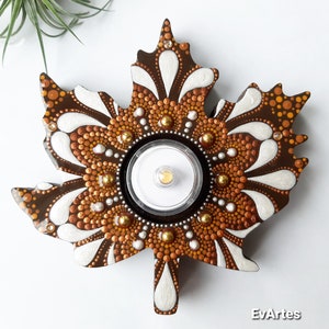 Könnte beinhalten: Ein Holzahornblatt, das mit einem Mandala-Design in Braun-, Gold- und Weißtönen bemalt ist. Die Mitte des Blattes hat einen runden Ausschnitt für ein Teelicht oder eine Votivkerze.