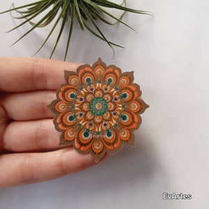 K&ouml;nnte beinhalten: Ein brauner Mandala-Aufkleber mit orangefarbenen, gr&uuml;nen und braunen Akzenten. Der Aufkleber hat die Form einer Blume mit einem kreisf&ouml;rmigen Design in der Mitte.