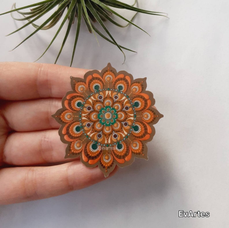 K&ouml;nnte beinhalten: Ein brauner Mandala-Aufkleber mit orangefarbenen, gr&uuml;nen und braunen Akzenten. Der Aufkleber hat die Form einer Blume mit einem kreisf&ouml;rmigen Design in der Mitte.