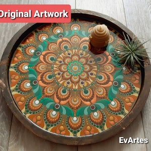 K&ouml;nnte beinhalten: Ein Holztablett mit einem braunen, gr&uuml;nen und goldenen Mandala-Design, das auf der Innenseite bemalt ist. Das Tablett hat eine klare Epoxidharz-Oberfl&auml;che und eine wabenf&ouml;rmige Kerze obenauf.