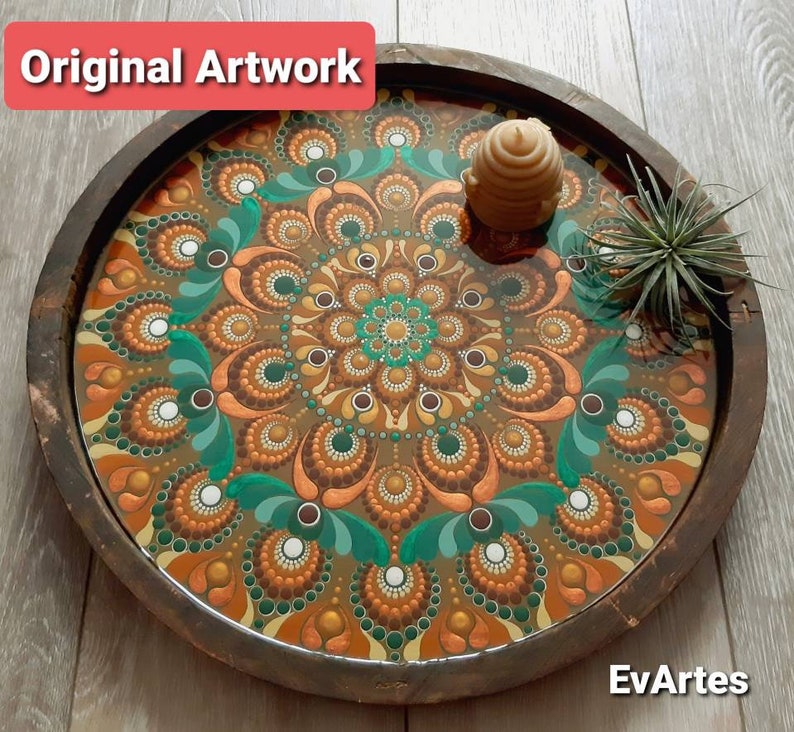 K&ouml;nnte beinhalten: Ein Holztablett mit einem braunen, gr&uuml;nen und goldenen Mandala-Design, das auf der Innenseite bemalt ist. Das Tablett hat eine klare Epoxidharz-Oberfl&auml;che und eine wabenf&ouml;rmige Kerze obenauf.