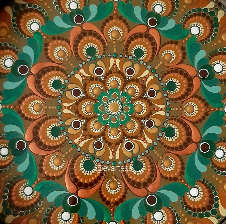 K&ouml;nnte beinhalten: Ein kreisf&ouml;rmiges Mandala-Design, das mit braunen, goldenen, gr&uuml;nen und wei&szlig;en Punkten bemalt ist. Das Mandala hat eine zentrale Bl&uuml;tenform mit acht Bl&uuml;tenbl&auml;ttern.