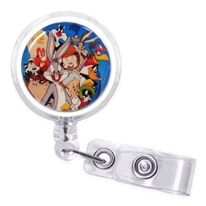 May include: A clear plastic badge holder with a round, colorful image of cartoon characters including Bugs Bunny, Daffy Duck, Tweety Bird, and Sylvester the Cat. The badge holder has a clear plastic clip and a retractable cord.