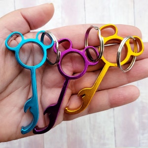 Puede incluir: Tres llaveros con abridor de botellas y accesorios de bucle. Los llaveros tienen forma de orejas de Mickey Mouse y son de color azul, morado y dorado.