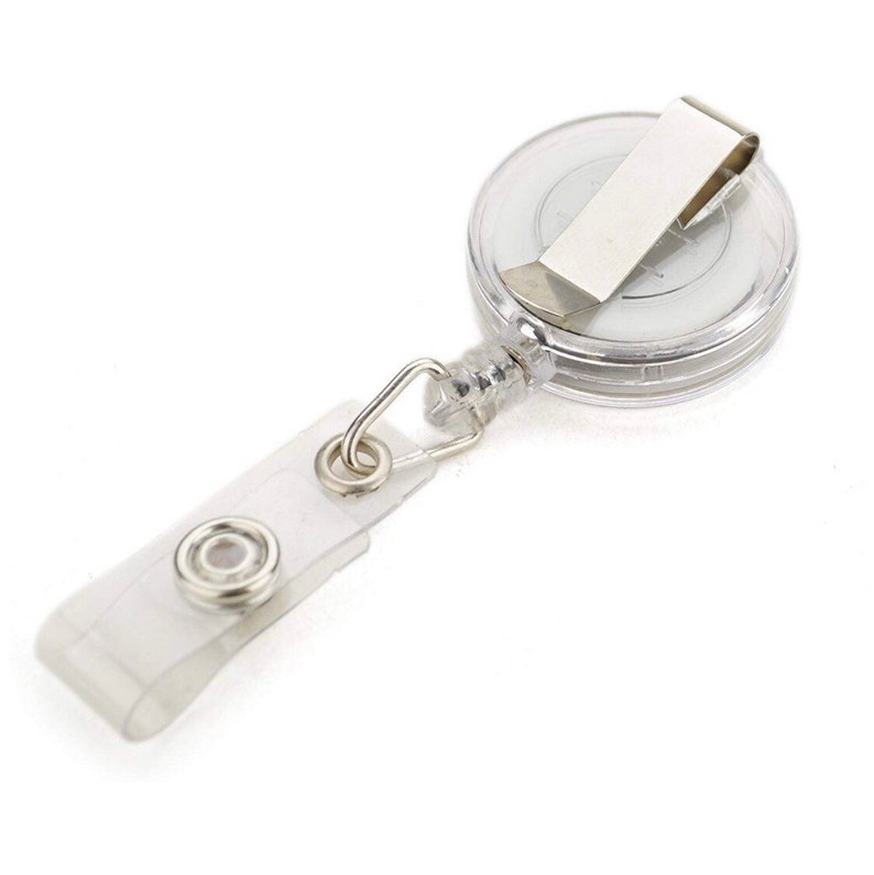 Op de afbeelding: Een transparante intrekbare badgehouder met een zilveren clip en een transparante plastic band. De houder heeft een veermechanisme waardoor de band kan worden uitgetrokken en ingetrokken.