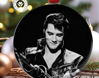 May include: Black and white photo of Elvis Presley playing a guitar. The photo is on a round, white ceramic ornament. The ornament has a red ribbon attached to the top.