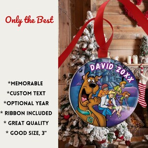 May include: Round Christmas ornament featuring Scooby-Doo and the gang in front of a haunted house. The ornament has a red ribbon for hanging and includes the text "DAVID 20XX". The ornament is 3 inches in diameter.