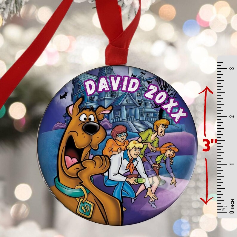 May include: A 3-inch round Christmas ornament featuring the Scooby-Doo gang in front of a haunted house. The ornament has a red ribbon for hanging and includes the text "DAVID 20XX". The ornament is a vibrant, colorful design.
