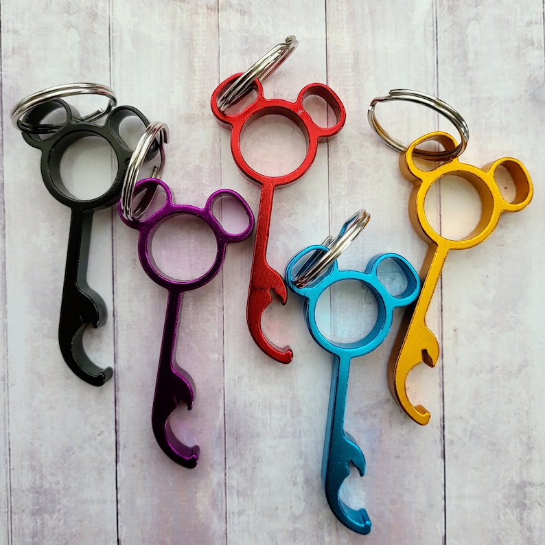 Puede incluir: Cinco abridores de botellas de diferentes colores con un dise&ntilde;o de cabeza de oso de dibujos animados. Los abridores de botellas est&aacute;n hechos de metal y tienen un anillo para sujetar a un llavero.