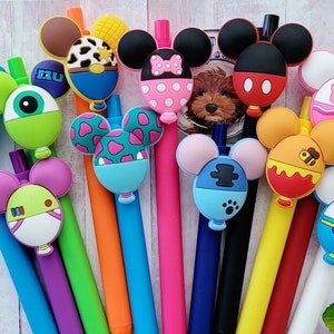 May include: A set of 12 colorful pens with different cartoon character toppers shaped like Mickey Mouse ears. The toppers feature various designs, including a monster, a bee, a cowboy, and a princess.