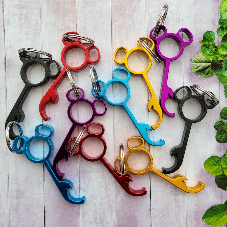 Puede incluir: Un conjunto de nueve abridores de botellas coloridos con un dise&ntilde;o de cabeza de Mickey Mouse. Cada abridor tiene un color diferente, incluyendo negro, rojo, azul, morado, dorado y plateado. Los abridores est&aacute;n hechos de metal y tienen un anillo para sujetar a un llavero.