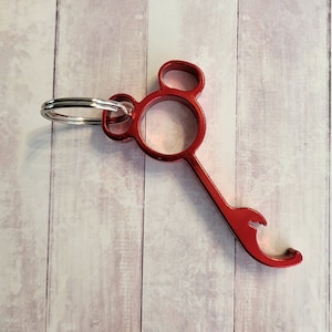 Puede incluir: Abrebotellas de metal rojo con un llavero y un dise&ntilde;o de cabeza de Mickey Mouse.