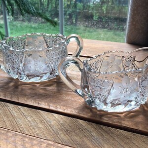 May include: A vintage glass sugar bowl and creamer set with a floral etched design. The set is clear glass with a delicate floral pattern.
