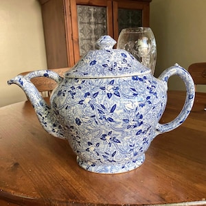 Peut inclure: Une théière à motifs floraux bleus et blancs avec un couvercle assorti. La théière a une anse et un bec courbés et repose sur une table en bois. La théière est de conception classique.