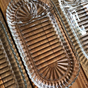 May include: Three clear glass serving dishes with a decorative, scalloped edge. The dishes have a raised, ribbed design and a smaller, fan-shaped section at one end.