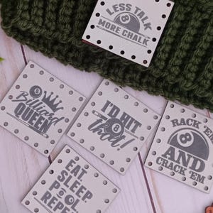 May include: A green and white crocheted beanie with a faux fur pom-pom. The beanie has a tag that says "LESS TALK MORE CHALK". There are also several tags with pool-related phrases.