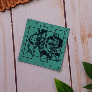 May include: A teal-colored, square-shaped patch featuring four horror movie characters. The patch has small holes around the edges. Above the patch is a wooden sign with the text "@WeatheredWeaves".