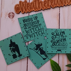 May include: Four teal-colored square tags with black witch-themed graphics and text. One tag reads "Buckle up Buttercup you just flipped my witch switch." Another says "Salem Broom Co." The tags are on a light wood surface with a wooden sign that says "@WeatheredWeaves".