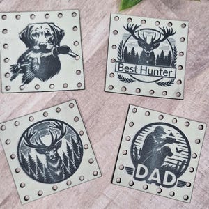 Op de afbeelding: Vier vierkante houten onderzetters met jachtontwerpen. Eén toont een hond met een eend, een andere zegt "Best Hunter" met een hert, een derde heeft een hert in een bos, en de laatste zegt "DAD" met een jager. Een houten bord met de tekst "@WeatheredWeaves" is ook aanwezig.