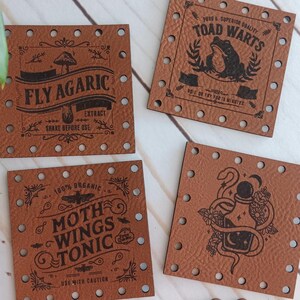 May include: Four square, brown leather labels with decorative text and illustrations. The labels read "FLY AGARIC EXTRACT", "TOAD WARTS", "MOTH WINGS TONIC", and a label with a snake and potion bottle. The wooden sign below reads "Weathered Weaves".