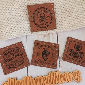 May include: A collection of brown leather tags with various designs and text, including "Unfiltered Poison" with a skull, "Unicorn Blood Fantasy Forest Potions & Poisons", "Love Potion No. 9", and "Phoenix Feathers". A wooden sign reads "@WeatheredWeaves".