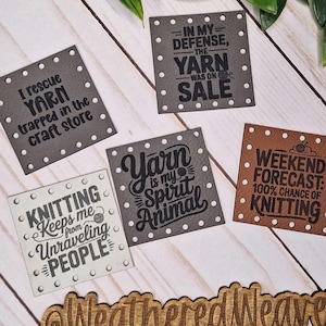 May include: A selection of square tags with witty sayings about yarn and knitting. The tags are in shades of grey and brown, with phrases such as "Knitting keeps me from unraveling people." The tags are for craft enthusiasts.