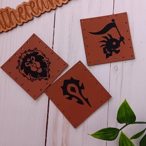 May include: Three brown leather patches with black embroidered designs. The designs are a lion's head, a stylised 'H' with a blade, and a goblin holding a flag.