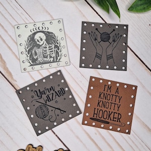 May include: Four square leather tags with white stitching. Designs include a skeleton, hands holding yarn, the words "Yarn Wizard", and "I'm a Knotty Knotty Hooker". A wooden sign with "Weathered Weaves" is at the bottom.