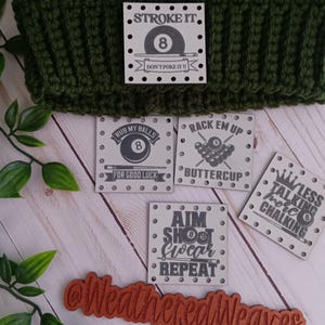 May include: A green and white crocheted beanie with a square patch that says "STROKE IT" with an image of an eight ball. There are also several square patches with pool-related phrases like "RUB MY BALLS" and "AIM SHOOT SCORE REPEAT".