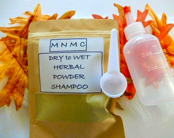Peut inclure: Un sachet en papier brun avec une étiquette indiquant "MNM C DRY to WET HERBAL POWDER SHAMPOO". Le sachet est à côté d'une bouteille en plastique transparente avec une cuillère doseuse blanche. La bouteille a un bouchon rouge et des marques pour les onces.