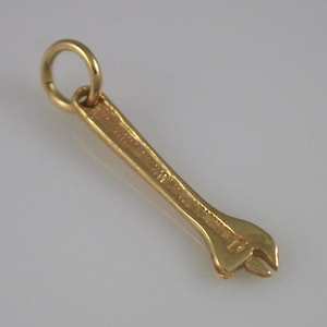 May include: A gold-coloured wrench charm with a circular loop at the top. The wrench has a detailed design and a small opening at the end. The charm is likely made of metal and is suitable for jewellery making.