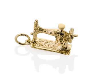 May include: A gold-colored charm in the shape of a vintage sewing machine. The charm has intricate details, including a wheel, needle arm, and base. The charm is designed to be attached to a necklace or bracelet.