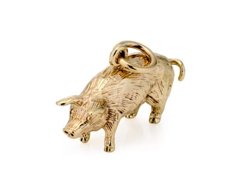 May include: A gold-colored pig charm with a textured surface. The pig is standing with its head down and has a loop at the top for attaching to a necklace or bracelet. The charm is a detailed representation of a pig.