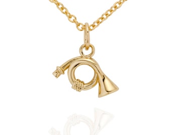 May include: A gold-colored necklace featuring a pendant shaped like a French horn. The pendant is suspended from a delicate chain. The French horn pendant has detailed curves and a polished finish, reflecting light. The necklace is suitable for music lovers.