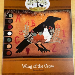 May include: A book cover with a brown background and a black crow with a white pear and pumpkins. The title is "Wing of the Crow" and the subtitle is "Autumn Book 1".