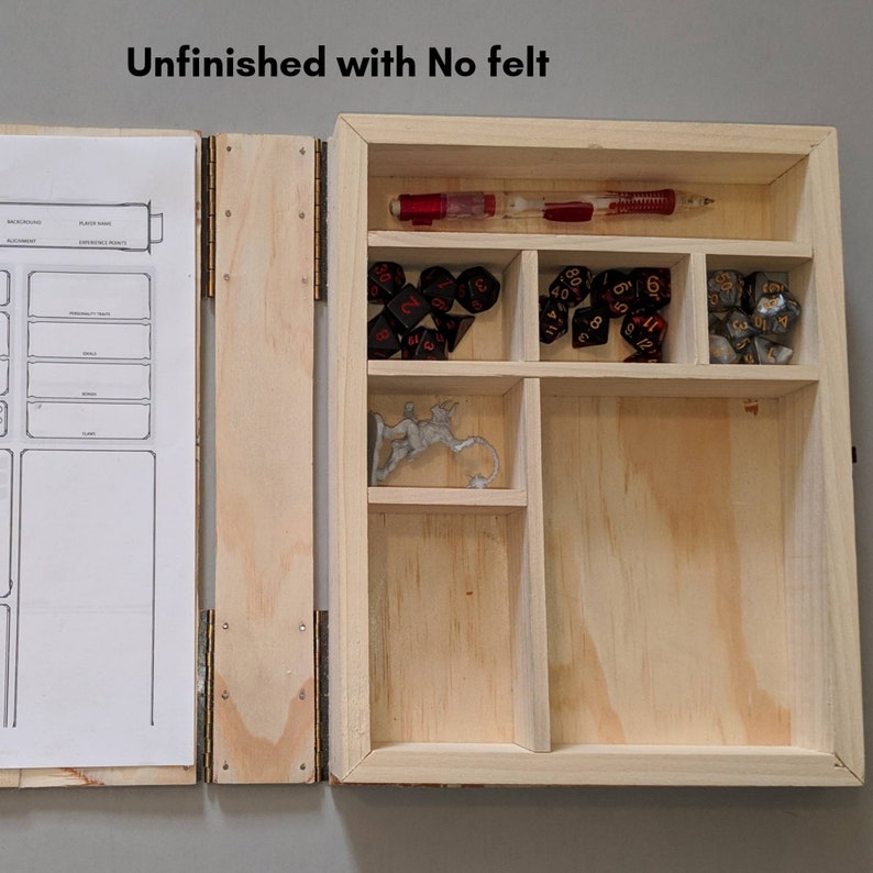 May include: Unfinished wooden box with compartments for dice and a miniature figure. The box is open and the compartments are empty except for the dice and figure. The box is made of light wood and has a natural finish. The text "Unfinished with No felt" is written on the top of the box.