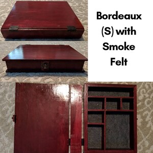 May include: A wooden box with a hinged lid and a felt-lined interior. The box is stained a deep red color and has a small brass lock on the front. The text "Bordeaux (S) with Smoke Felt" is visible on the right side of the image.