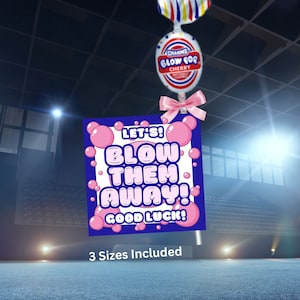 May include: A pink and blue sign with the text "Let's! Blow Them Away! Good Luck!" and pink bubble graphics. The sign is attached to a lollipop with a white wrapper and a red, white, and blue striped top. The text "3 Sizes Included" is below the sign.