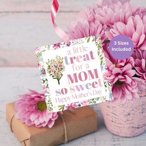 May include: A white gift tag with a floral border and the text "a little treat for a MOM so sweet Happy Mother's Day". The tag is tied with a pink ribbon and is hanging from a bouquet of pink flowers.