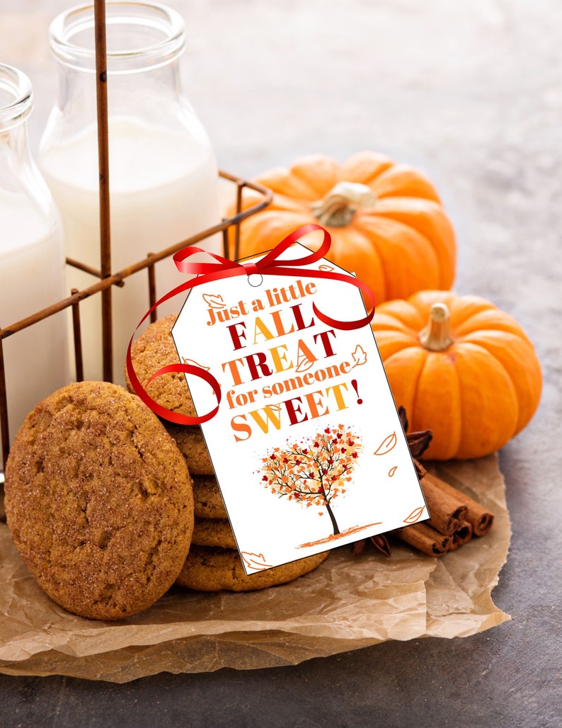 Op de afbeelding: Een wit cadeau-etiket met een rood lint eromheen, met de tekst "Just a little FALL TREAT for someone SWEET!" en een herfstboomillustratie. Het etiket ligt op een stapel peperkoekjes, twee mini-pompoenen, kaneelstokjes en steranijs op bruin perkamentpapier.
