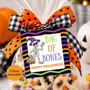 May include: A clear plastic treat bag filled with white chocolate-covered pretzels decorated with small colorful bone-shaped sprinkles. The bag is tied with an orange polka dot and black and white gingham ribbon and a tag reading BAG OF BONES.